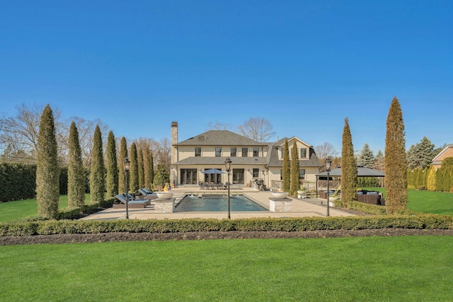 rear view of house featuring a patio area, a gazebo, a chimney, an outdoor pool, and a yard