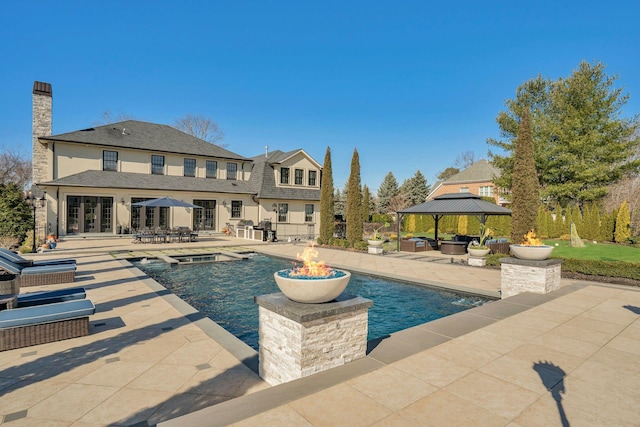 outdoor pool with french doors, area for grilling, a gazebo, an outdoor living space with a fire pit, and a patio area