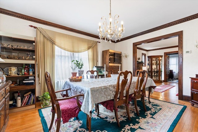 dining area with a notable chandelier, light wood-type flooring, and ornamental molding