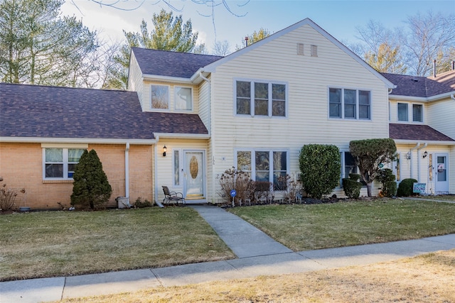 traditional home featuring roof with shingles, brick siding, and a front lawn