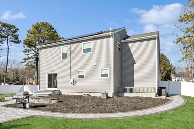 back of house with entry steps, solar panels, central AC, fence, and a gate