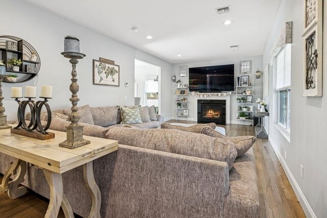 living room featuring baseboards, visible vents, a glass covered fireplace, wood finished floors, and recessed lighting