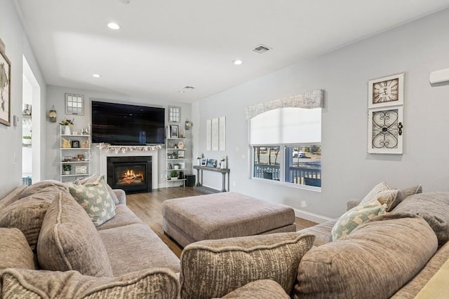 living area with recessed lighting, visible vents, a glass covered fireplace, wood finished floors, and baseboards