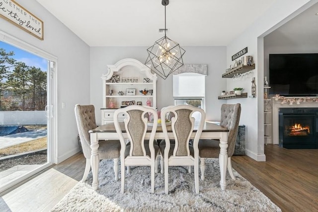 dining room featuring a chandelier, a fireplace with flush hearth, wood finished floors, and baseboards