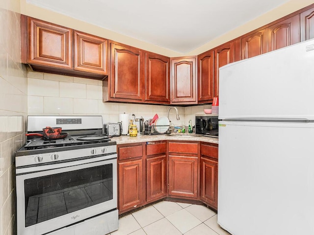 kitchen featuring stainless steel gas stove, light tile patterned floors, tasteful backsplash, and freestanding refrigerator