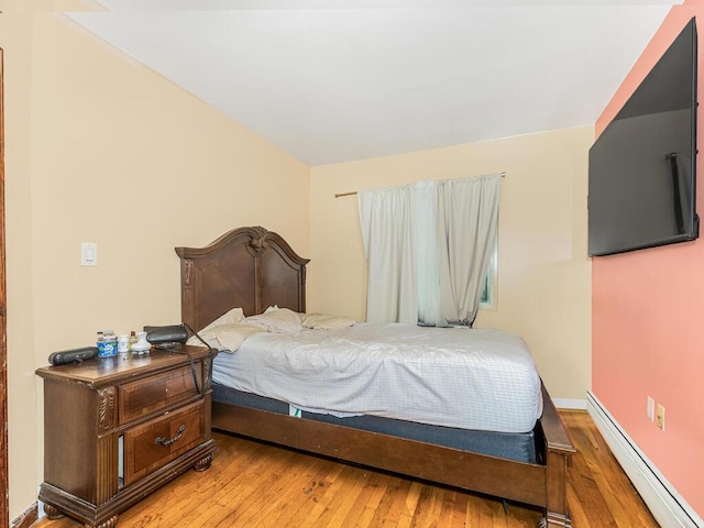 bedroom with a baseboard heating unit, baseboards, and hardwood / wood-style floors