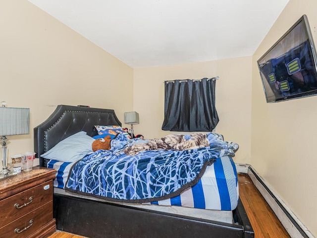 bedroom featuring a baseboard heating unit, baseboards, and wood finished floors