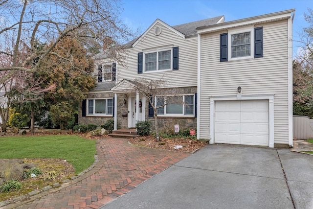 traditional-style house featuring stone siding, decorative driveway, an attached garage, and a front yard