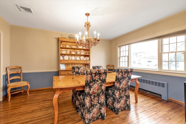 dining area with visible vents, radiator, ornamental molding, hardwood / wood-style floors, and a notable chandelier