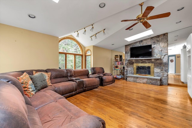 living room featuring lofted ceiling with skylight, ceiling fan, a fireplace, and light wood finished floors