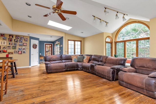 living room with ceiling fan, vaulted ceiling with skylight, and light wood-style flooring