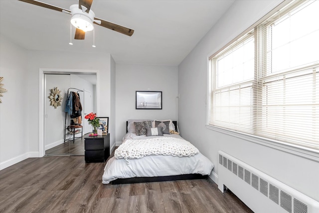 bedroom with wood finished floors, a ceiling fan, baseboards, a closet, and radiator