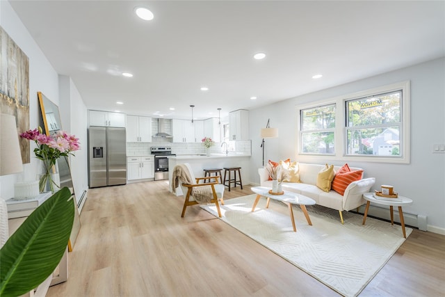 living area with a baseboard radiator, light wood-style flooring, baseboards, and recessed lighting