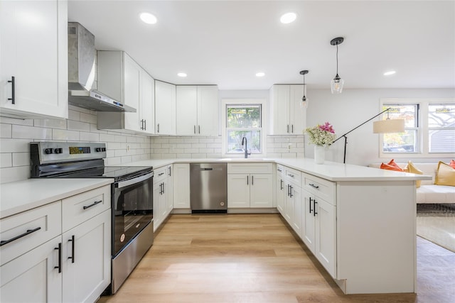 kitchen featuring white cabinets, appliances with stainless steel finishes, a peninsula, wall chimney range hood, and a sink