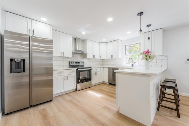 kitchen with tasteful backsplash, wall chimney exhaust hood, a peninsula, stainless steel appliances, and light wood-style floors