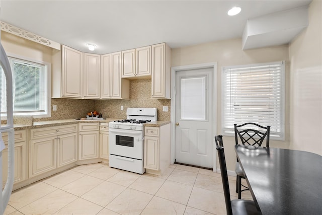 kitchen featuring cream cabinetry, tasteful backsplash, light tile patterned flooring, white range with gas cooktop, and a sink