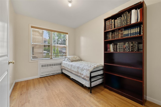 bedroom featuring radiator heating unit, light wood-style flooring, and baseboards