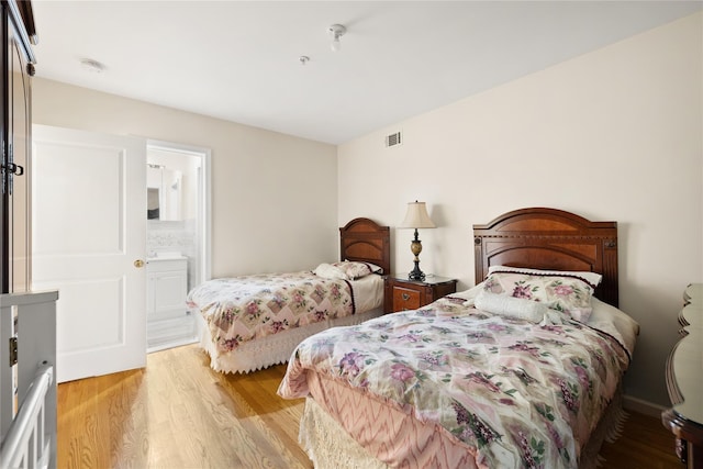 bedroom with ensuite bathroom, light wood-type flooring, and visible vents