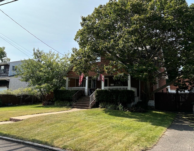 view of property hidden behind natural elements with a porch, fence, and a front lawn