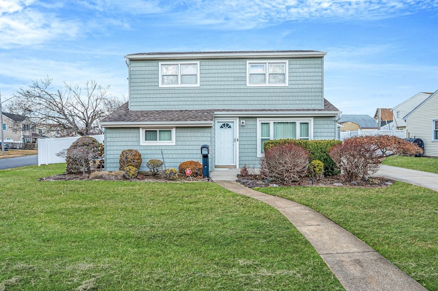 traditional-style house with a front lawn, a shingled roof, and fence