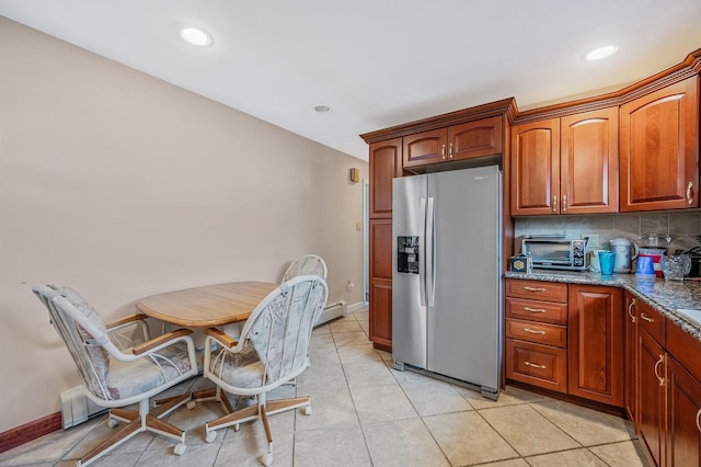 kitchen featuring light tile patterned floors, stainless steel fridge, a toaster, tasteful backsplash, and dark stone countertops