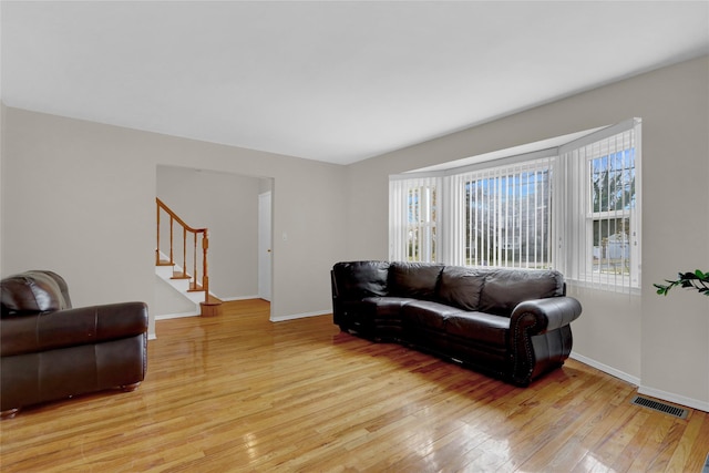 living room with light wood-type flooring, visible vents, baseboards, and stairs