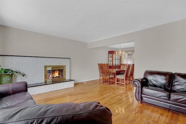 living room featuring a chandelier, a fireplace, light wood-style flooring, and baseboards