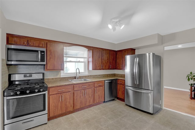 kitchen with tasteful backsplash, baseboards, appliances with stainless steel finishes, brown cabinets, and a sink