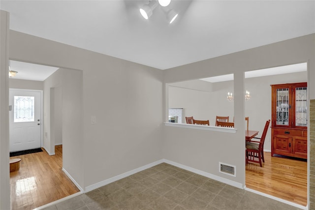 unfurnished room with visible vents, a notable chandelier, light wood-style flooring, and baseboards