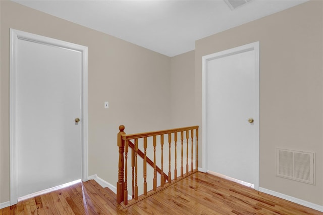 hall featuring light wood finished floors, an upstairs landing, visible vents, and baseboards