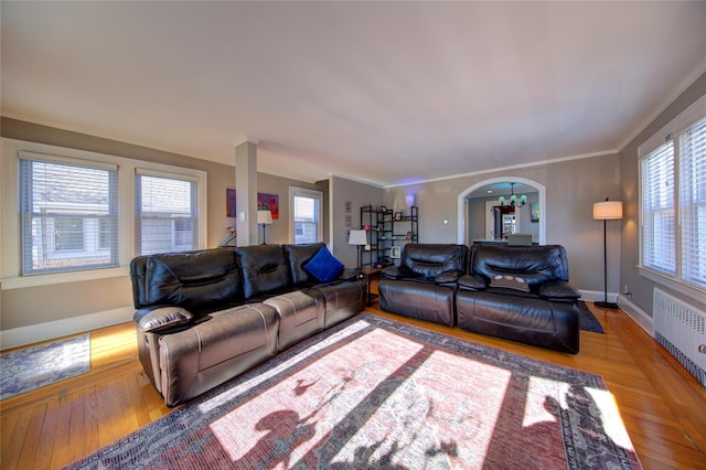 living area with light wood-type flooring, arched walkways, ornamental molding, and radiator heating unit