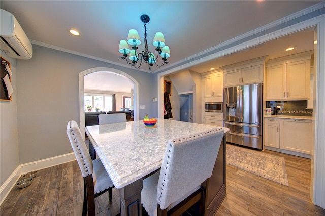 dining area featuring a wall mounted AC, ornamental molding, wood finished floors, a chandelier, and baseboards