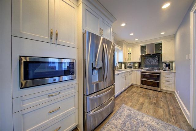 kitchen featuring dark wood finished floors, stainless steel appliances, recessed lighting, a sink, and wall chimney exhaust hood