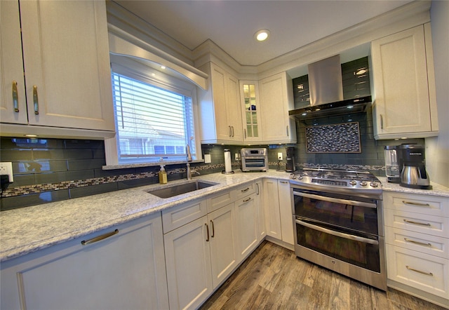 kitchen featuring wood finished floors, a sink, wall chimney range hood, double oven range, and backsplash