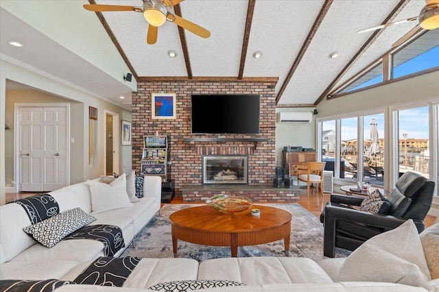 living room with ceiling fan, beamed ceiling, a textured ceiling, a brick fireplace, and a wall mounted AC