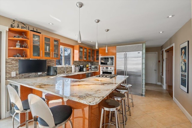 kitchen with built in appliances, a peninsula, a sink, backsplash, and brown cabinets