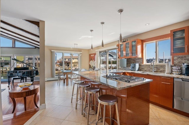 kitchen featuring stainless steel gas cooktop, a kitchen island, a sink, brown cabinets, and decorative backsplash