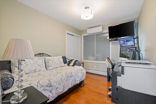 bedroom featuring a closet, a baseboard radiator, an AC wall unit, and wood finished floors