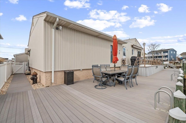 wooden terrace featuring outdoor dining area, fence, and a gate