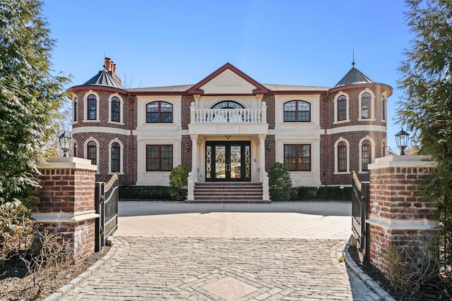 view of front facade featuring a balcony, a chimney, french doors, decorative driveway, and brick siding