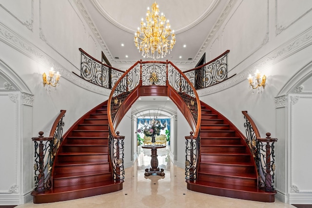 stairway with a notable chandelier, marble finish floor, ornamental molding, arched walkways, and a high ceiling