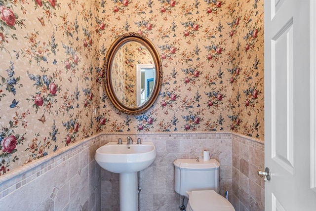 bathroom with a wainscoted wall, toilet, wallpapered walls, and tile walls