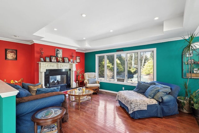 living area featuring ornamental molding, a tray ceiling, a glass covered fireplace, and hardwood / wood-style flooring