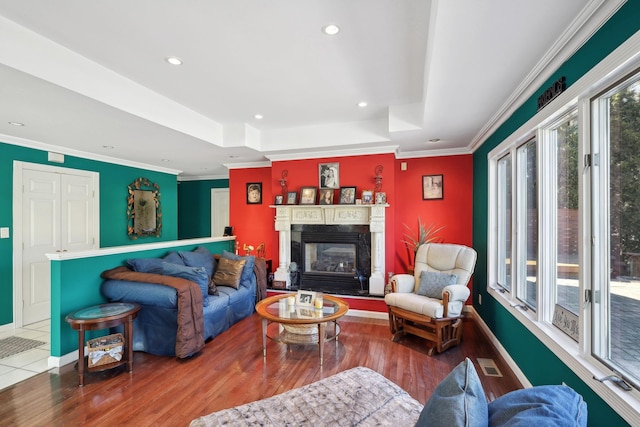 living area featuring crown molding, visible vents, a glass covered fireplace, wood finished floors, and baseboards