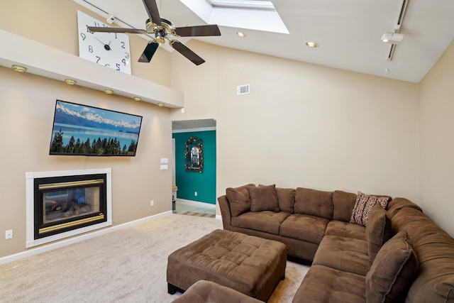 living room featuring a skylight, visible vents, baseboards, carpet, and a glass covered fireplace