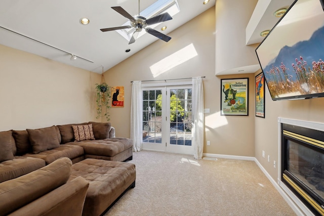 carpeted living area with high vaulted ceiling, a skylight, baseboards, a glass covered fireplace, and rail lighting