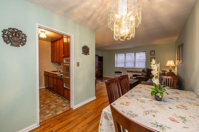 dining area with baseboards, radiator, light wood finished floors, and an inviting chandelier