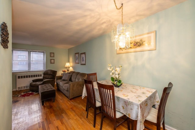 dining area featuring radiator heating unit, wood-type flooring, and a notable chandelier