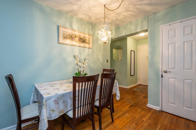 dining area featuring baseboards, hardwood / wood-style floors, and an inviting chandelier