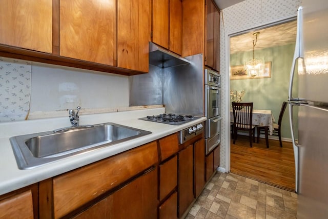 kitchen featuring brown cabinets, light countertops, an inviting chandelier, appliances with stainless steel finishes, and a sink